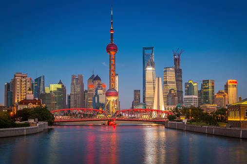 The iconic spire of the Oriental Pearl Tower and futuristic skyscrapers of Shanghai's Pudong financial district overlooking the historic trusses of Waibaidu Bridge under deep blue dusk skies, China. ProPhoto RGB profile for maximum color fidelity and gamut.