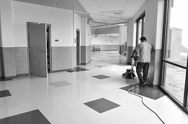 A custodial worker buffing (Waxing) floors using an electrical buffer. Black and white.