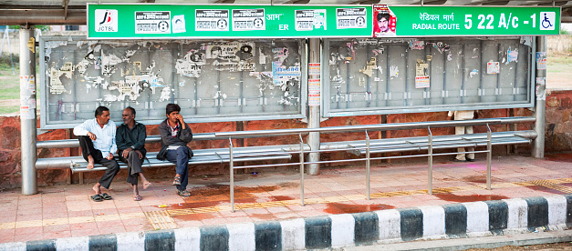 Jaipur, Rajasthan, India - March 7, 2015. Three Indian men sitting on a bench at a bus stop waiting for a bus in Jaipur, India. 