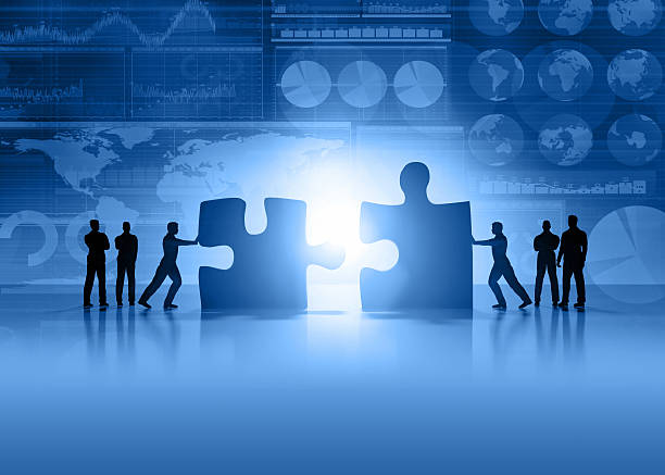 Business teamwork and global finance blue background Silhouette of business people moving and joining pieces of jigsaw puzzle on a business and stock market blue background, with charts, diagrams, world maps and data arranged on grid and tables. World maps showing continents and countries with economy data and growth diagrams. Light glowing from the center. Copy space on bottom. mergers and acquisitions stock pictures, royalty-free photos & images