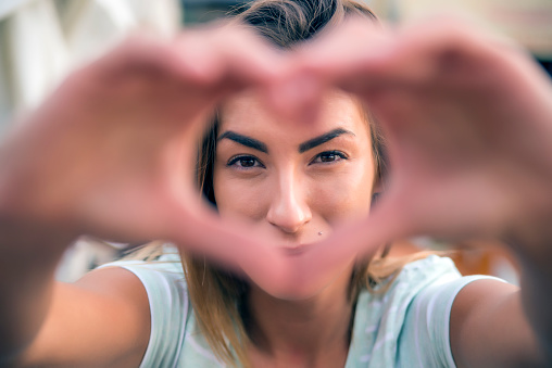 Young cute woman with smiley face making heart shape by her hands