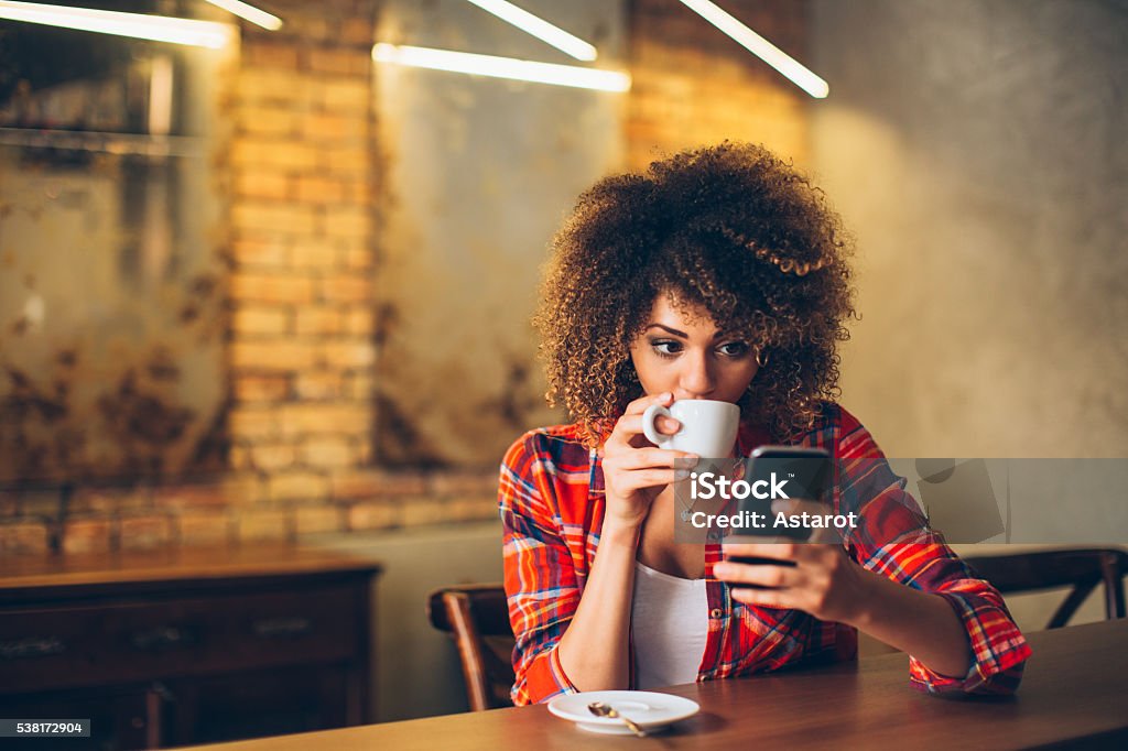 Woman using mobile phone Young woman at cafe drinking coffee and using mobile phone Mobile Phone Stock Photo