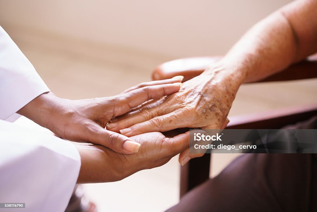 Senior Woman Talking With Black Doctor In Hospice Old people in geriatric hospice: Aged patient receives the visit of a female black doctor. They shake their hands and talk in the hospital. Senior Adult Stock Photo