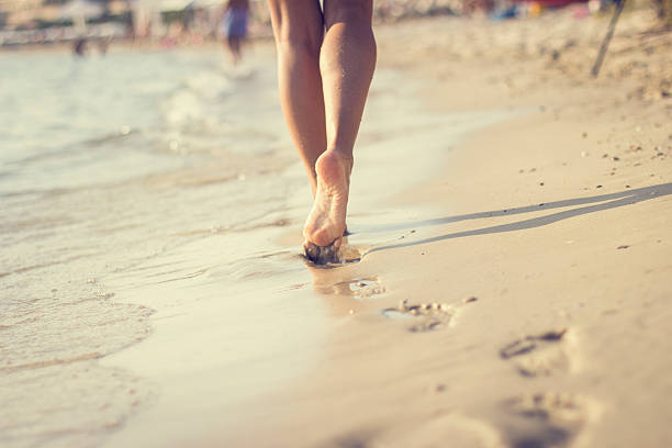Woman walking on sand beach leaving footprints in the sand