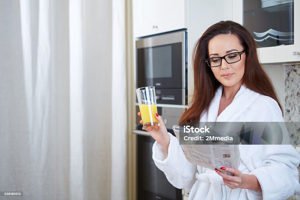 Woman reading the news while drinking orange juice Woman reading the news while drinking orange juice in her kitchen 2015 Stock Photo