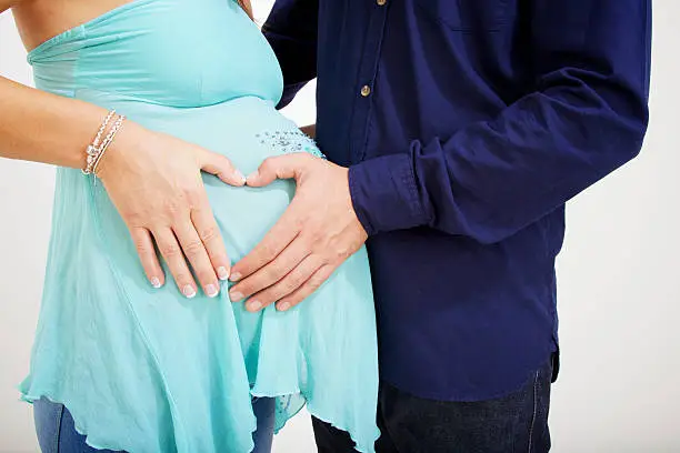 a headless shot of a heavily pregnant woman as she cuddles her partner who is embracing the bump