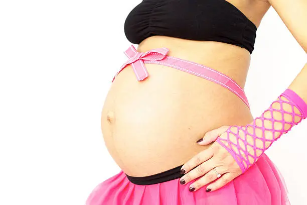 A studio shot showing a pregnant tummy adorned with 80's style neon pink gloves and skirt to showcase the gender of the baby