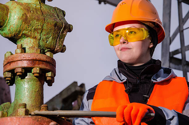 Woman in the oilfield Woman engineer in the oil field repairing wellhead with the wrench wearing orange helmet and work clothes. Oil and gas concept. wellhead stock pictures, royalty-free photos & images