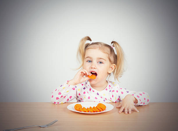 ��小さな女の子 食べる ニンジンと分岐点があります。 - cute disgust carrot caucasian ストックフォトと画像