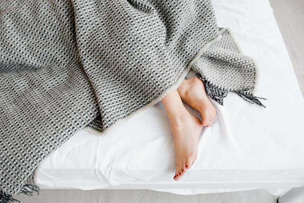 donna piedi sotto una coperta a gettare - bed human leg home interior comfortable foto e immagini stock