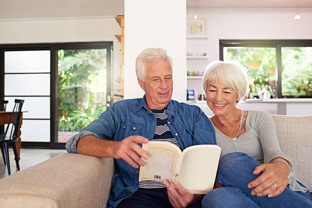 In between the pages of a book of love Shot of a relaxed senior couple reading a book together on the sofa at home real wife stories stock pictures, royalty-free photos & images