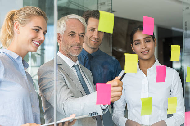 Business team looking at sticky notes Professional business team discussing ideas on sticky notes. Businessman showing written work on sticky notes. Creative team discussing over adhesive notes. cfo stock pictures, royalty-free photos & images