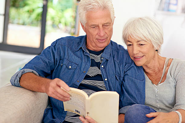 Living their very own love story Shot of a relaxed senior couple reading a book together on the sofa at home real wife stories stock pictures, royalty-free photos & images