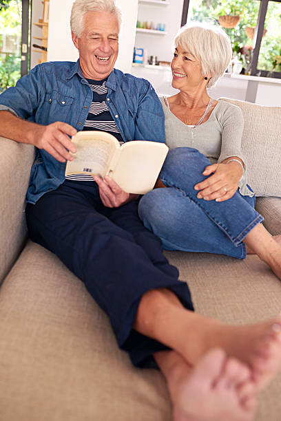 Real love stories do come true Shot of a relaxed senior couple reading a book together on the sofa at home real wife stories stock pictures, royalty-free photos & images
