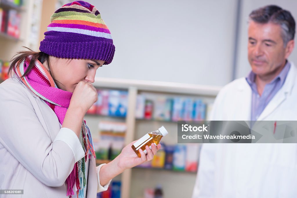 Sick woman holding a box of medicine Sick girl with scarf and colorful hat holding a bottle of drug in the pharmacy 20-24 Years Stock Photo