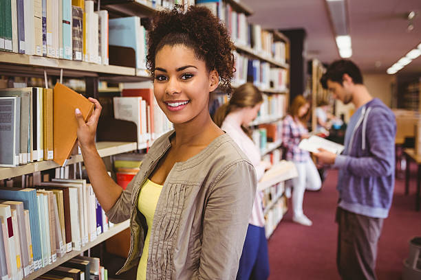 Smiling student picking out a book Smiling student picking out a book in library wavebreakmedia stock pictures, royalty-free photos & images