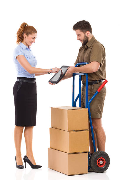 Please confirm a delivery Smiling office female worker receives delivery from messenger and tapping at digital tablet. Full length studio shot isolated on white. mover delivery person box hand truck stock pictures, royalty-free photos & images