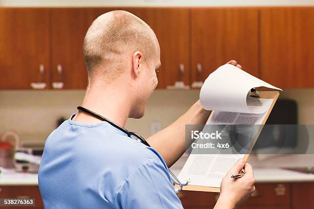 Male Doctor Looking At Clipboard In Hospital Stock Photo - Download Image Now - 2015, 30-34 Years, 30-39 Years