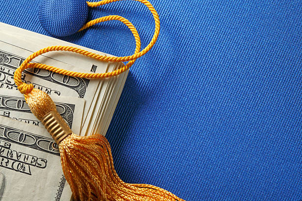 Student Loan Concept A stack of one hundred dollar bills on top of a blue graduation cap.  A gold graduation tassel is draped over the stack of money. The ledft side of image is available for copy. mortarboard photos stock pictures, royalty-free photos & images