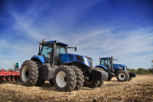 Two blue tractor with drills in the field under blue sky