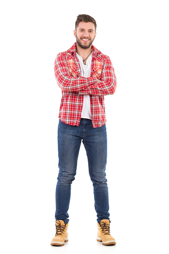 Handsome young man in jeans and lumberjack shirt standing with arms crossed. Full length studio shot isolated on white.