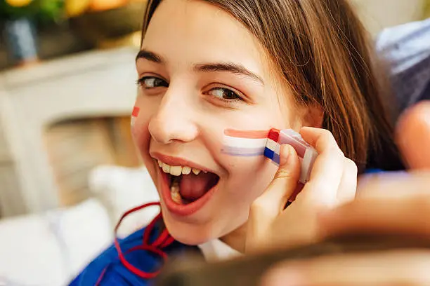 Photo of french teenage girl painting face with tricolore and taking selfie