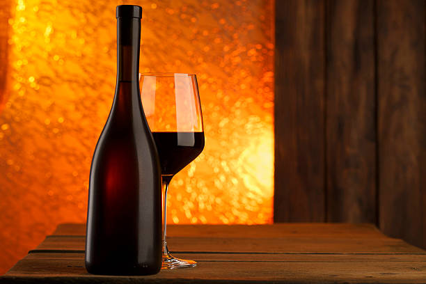 Red wine bottle and stylish wineglas.  Glasses of red wine standing on an old wooden table, warm sunset light penetrates through the window. The beautiful romantic atmosphere of the setting, calls for consummation. Shot with Canon 5DMarkIII, developed from RAW, Adobe RGB color profile. Shallow DOF for soft background.