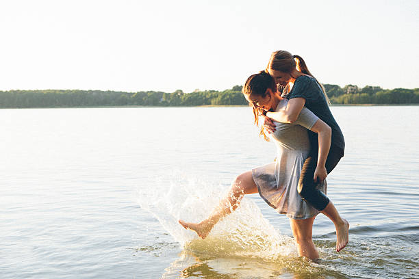 istock two young woman having fun with piggyback in lake, backlit 538324950