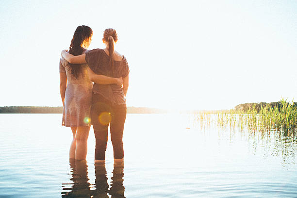istock rear view, two young woman looking the sunset over lake 538327672