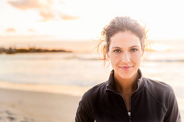 Confident sporty woman at beach A photo of fit young woman with confident look on her face. Portrait of happy female athlete is at beach. She is wearing sportswear during sunset. 30 34 years stock pictures, royalty-free photos & images