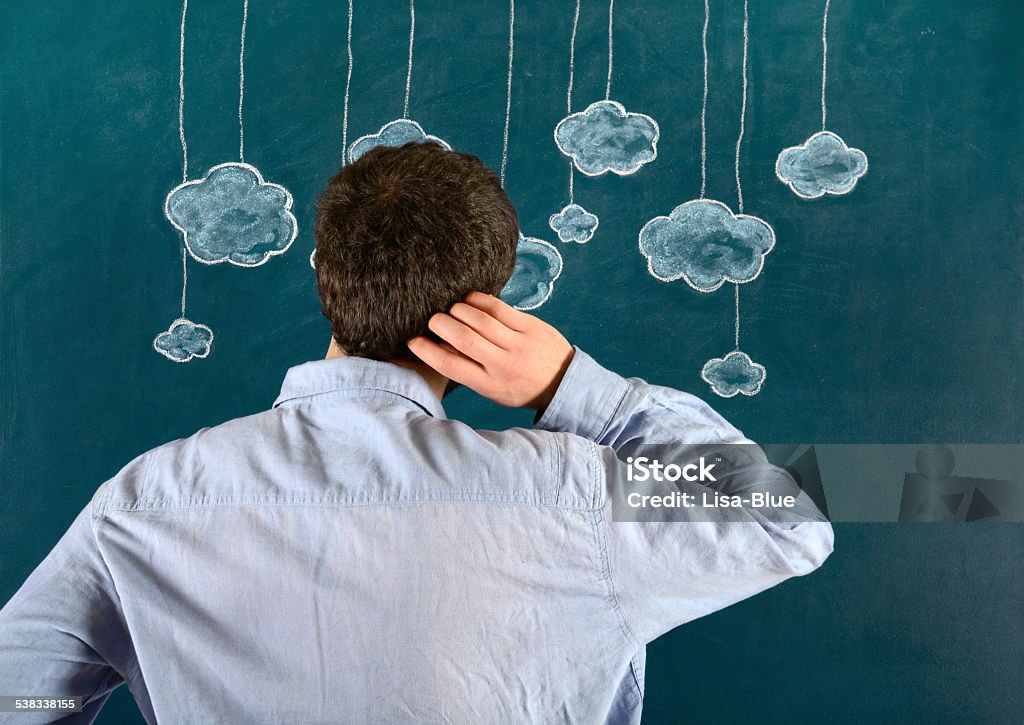 Cloud Computing Concept Pensive young man standing with his face in front of a blue blackboard. He is touching his hair and looking clouds. The chalkboard drawing - cloud computing concept - shows multiple clouds outlined in white and blue on a blue background. There are nine blue clouds of various sizes dangling from white strings attached to the top of the illustration. The blue background looks like a sky. 2015 Stock Photo