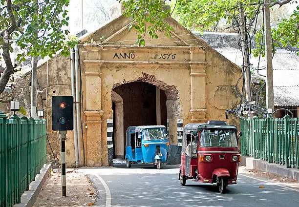 Auto-Rickshaws make their way under the old Dutch arch of Trincomalee Fort entrance as the traffic lights change in their favour, Sri Lanka