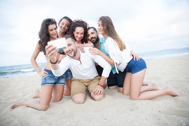 istock Group of cheerful friends kneeling on sand and making selfe 538351586