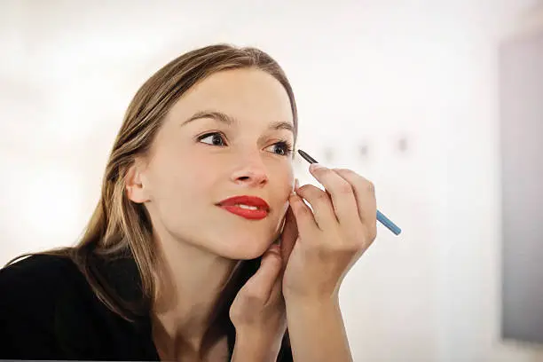beautiful woman putting make-up on looking in the mirror