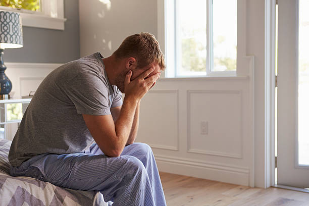 Man Wearing Pajamas Sitting On Bed With Head In Hands Man Wearing Pajamas Sitting On Bed With Head In Hands facepalm stock pictures, royalty-free photos & images