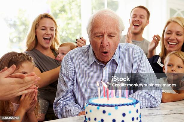 Grandfather Blows Out Birthday Cake Candles At Family Party Stock Photo - Download Image Now