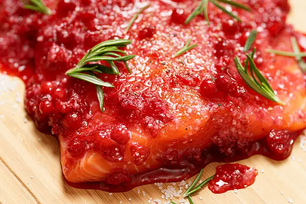 Salmon steak being marinated in salt with redberries and rosemary