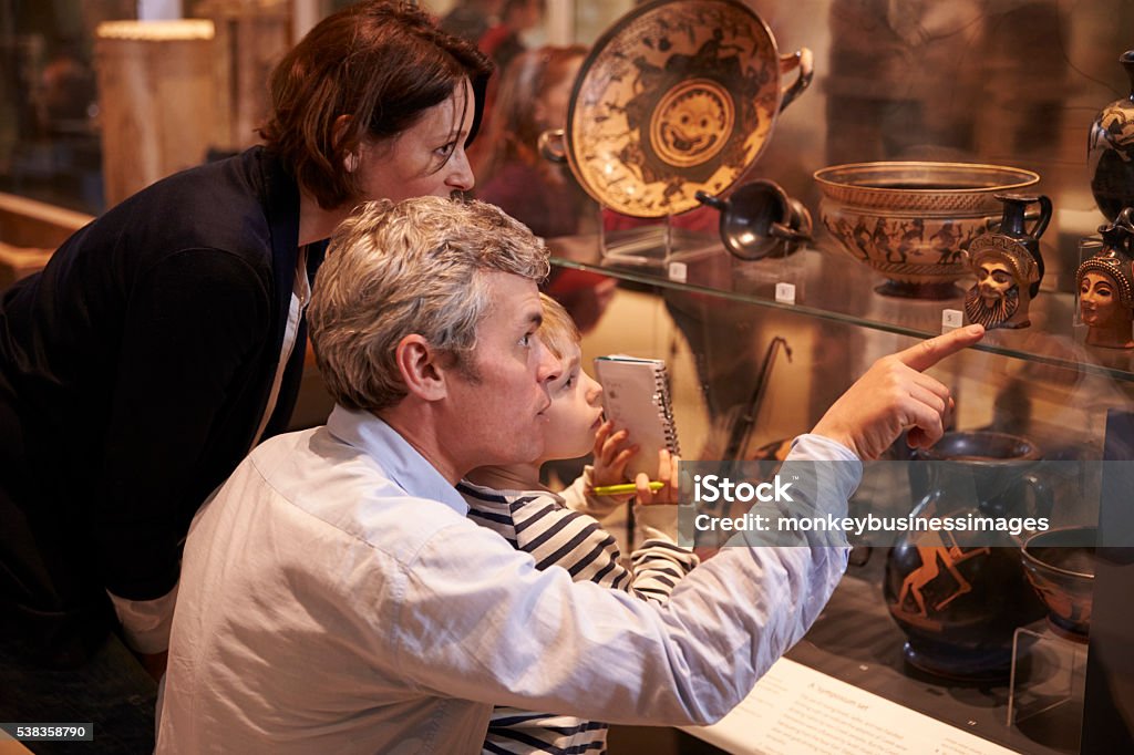 Family Looking At Artifacts In Glass Case On Trip Family Looking At Artifacts In Glass Case On Trip To Museum Museum Stock Photo