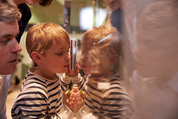 An 8 year old blonde autistic boy takes a break from a family gathering to look out the window as his reflection is mirrored in the granite countertop