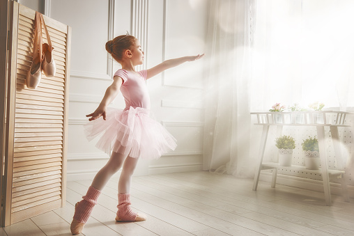 Cute little girl dreams of becoming a ballerina. Child girl in a pink tutu dancing in a room. Baby girl is studying ballet.