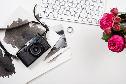 Modern computer keyboard, pink flowers and photo camera on white table, photographer girl's workspace