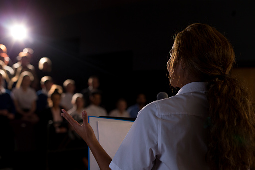 Female student making a speech. She is standing at a podium and talking to the crowd.