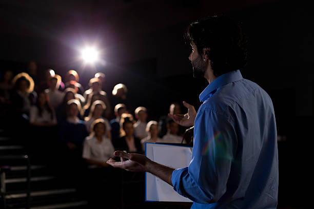 Making a Speech Male teacher giving a speech in a lecture hall to students and teachers. theater class stock pictures, royalty-free photos & images