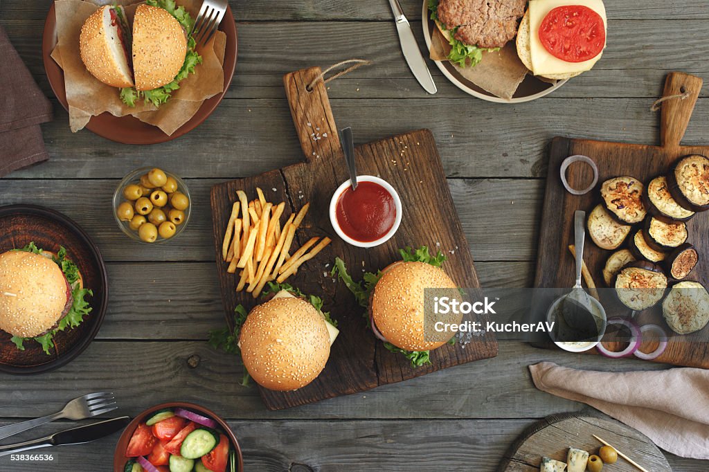 Burgers with different food Different food on a wooden table, burgers, fries, grilled eggplant, salad, different sauces and olives, top view. Outdoors food Concept Cafe Stock Photo