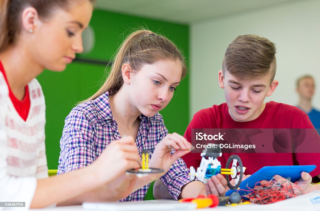 Teamwork in Lessons Students working together with a digital tablet to build a robot in a classroom. High School Stock Photo