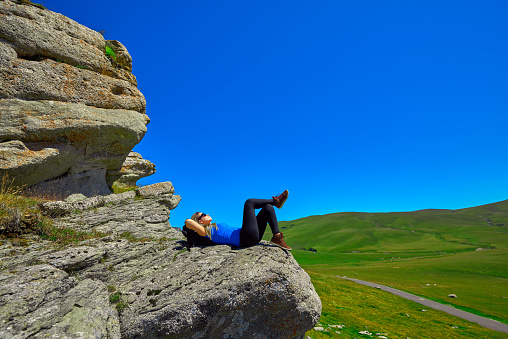 side view of hiker woman lying down on rock and relaxing, resting and feeling carefree.summer season, clear sky in background.