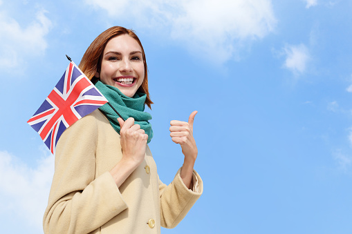 happy young travel woman holding British England flag with sky background, caucasian beauty