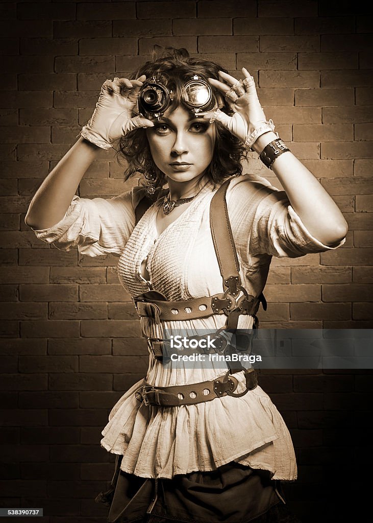 Redhair girl with steampunk goggles. Old-fashioned. Beautiful redhair girl with steampunk Goggles standing on a brick wall background and looking at the camera. Old-fashioned. Women Stock Photo