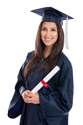 A young female graduate turns around as she poses for a portrait.  She is wearing a gown and cap and smiling proudly as she stands with her peers who have their backs to the camera.