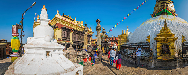 Kathmandu, Nepal - 7th November 2014: The iconic white stupas, golden shrines, colourful prayer flags, workers and visiting crowds of Swayambhunath, the Monkey Temple complex and sacred Buddhist pilgrimage site overlooking Kathmandu, Nepal's vibrant capital city. Composite panoramic image created from nine contemporaneous sequential photographs.